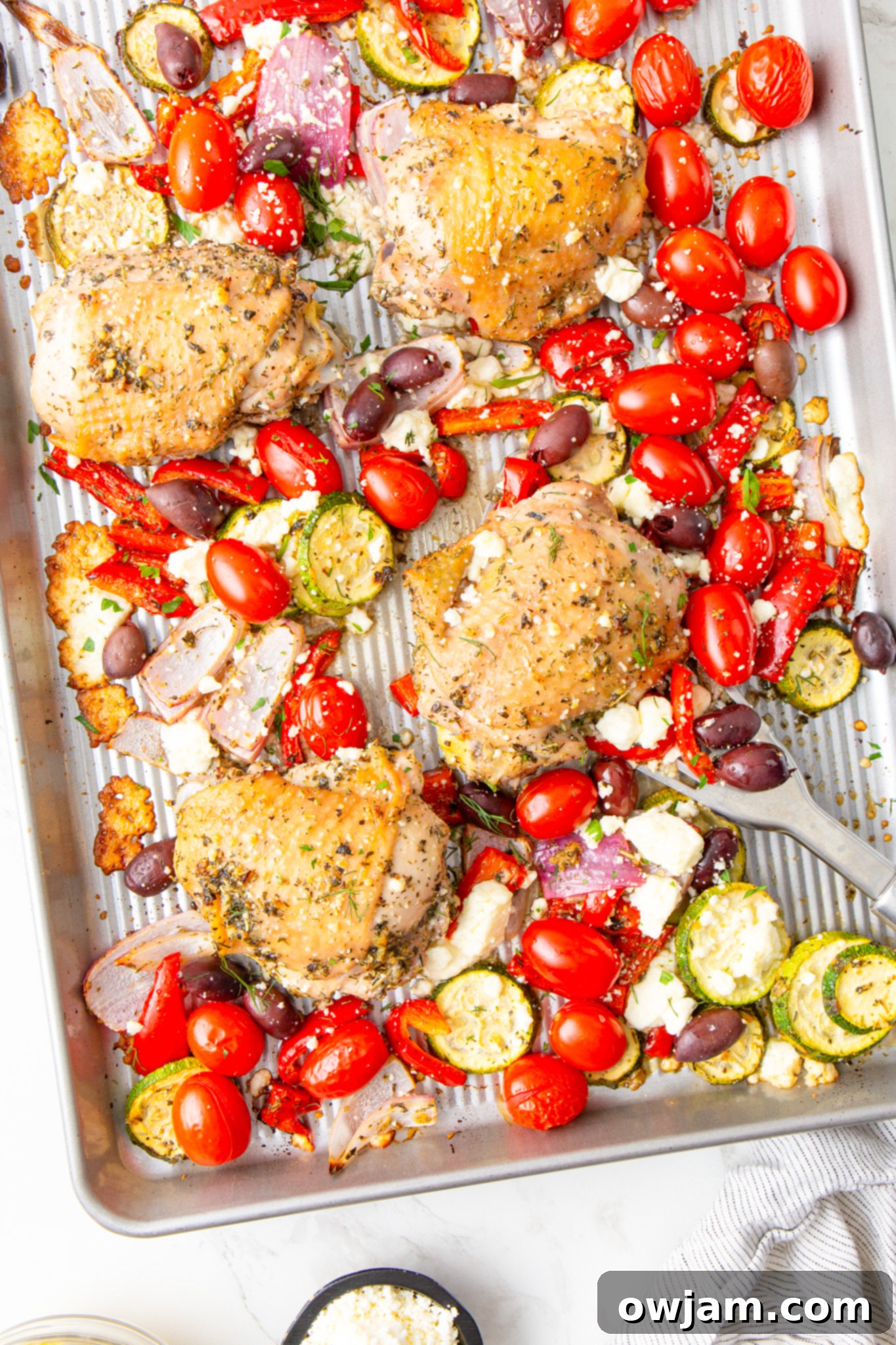 Mediterranean Sheet Pan Chicken 4 Mediterranean Sheet Pan Chicken in a bowl with a spoon, showing the perfectly roasted chicken and vegetables.