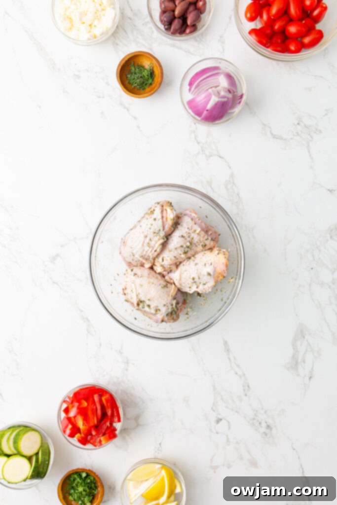 Mediterranean Sheet Pan Chicken 5 Chicken thighs marinating in a bowl with Mediterranean herbs and lemon.