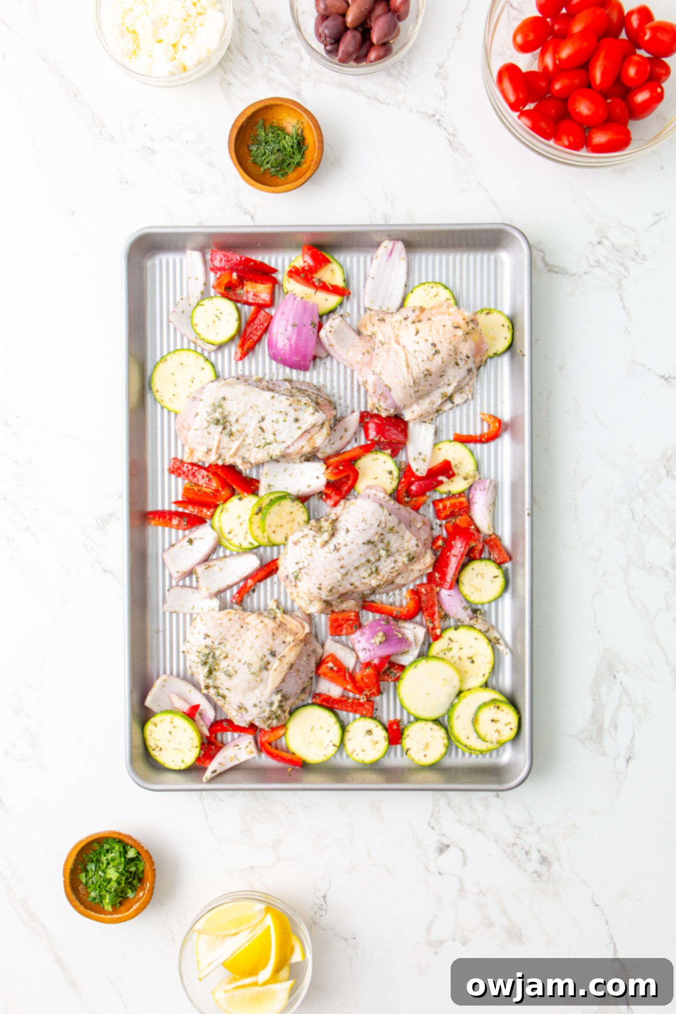Mediterranean Sheet Pan Chicken 8 Mediterranean Sheet Pan Chicken and vegetables arranged on a baking sheet before cooking.