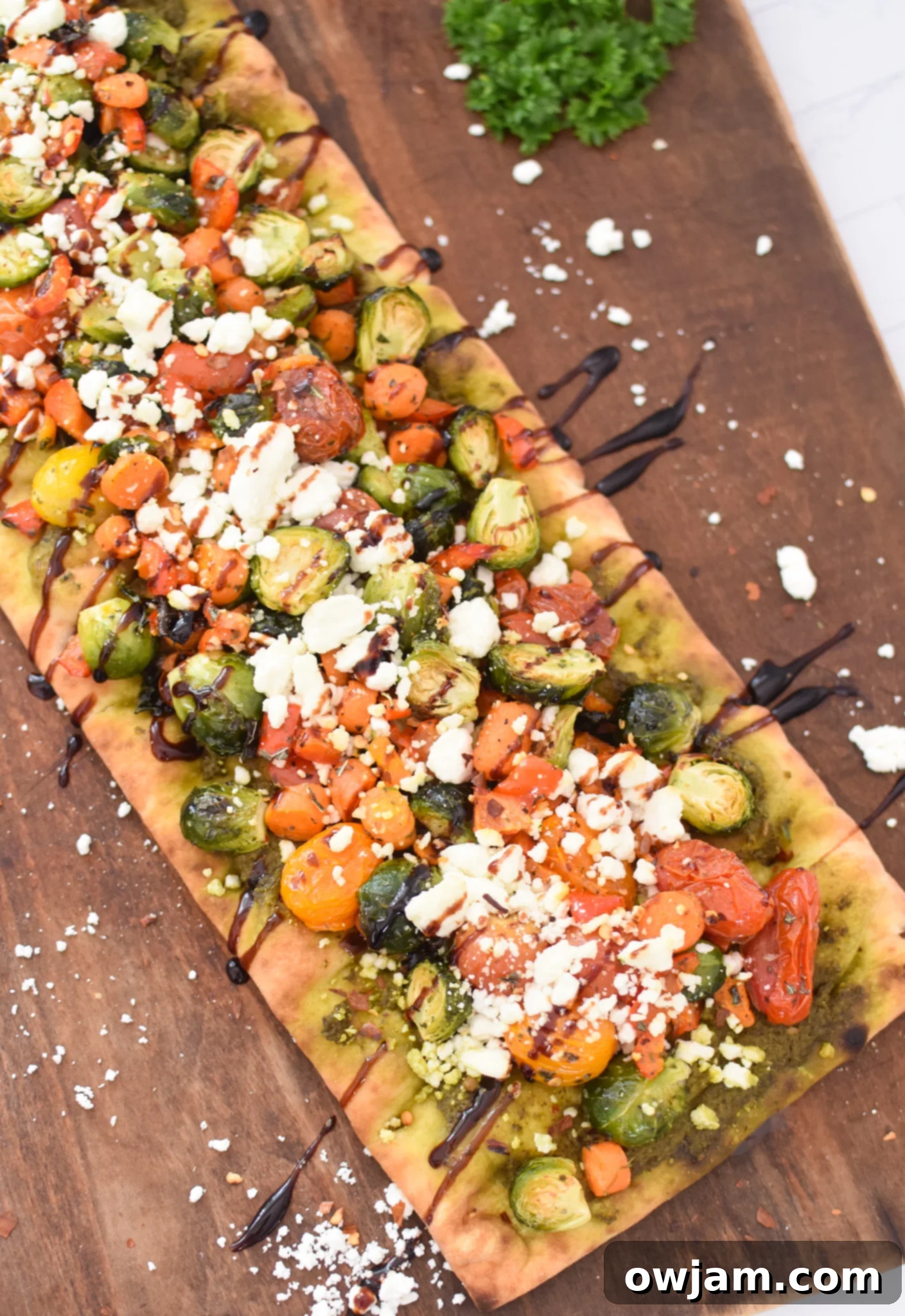 Roasted Vegetable Goat Cheese Flatbread Pizza Recipe on a cutting board, garnished with fresh herbs.