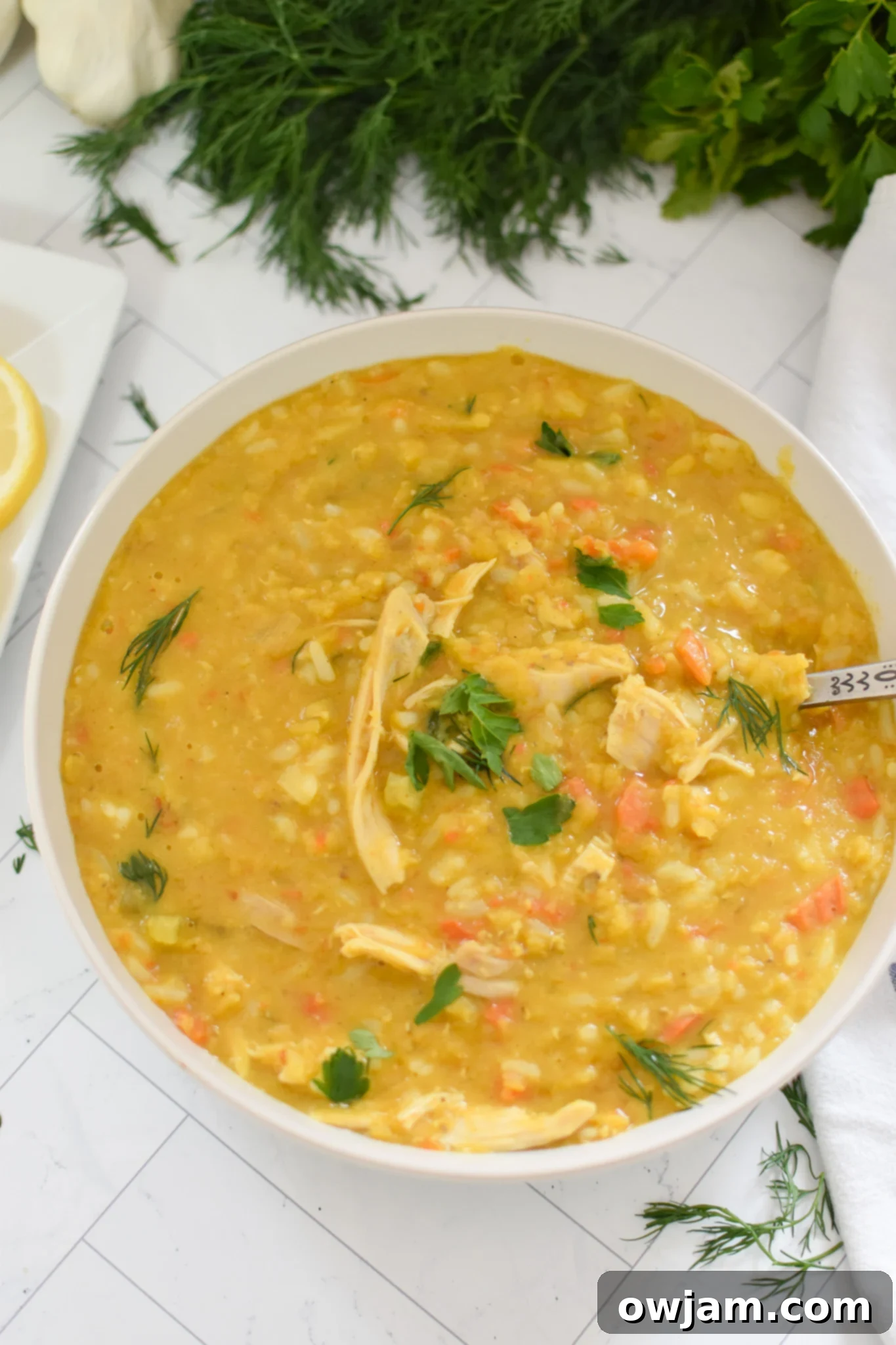 A single serving of Chicken Lentil Soup in a white bowl with a spoon, garnished with fresh herbs.