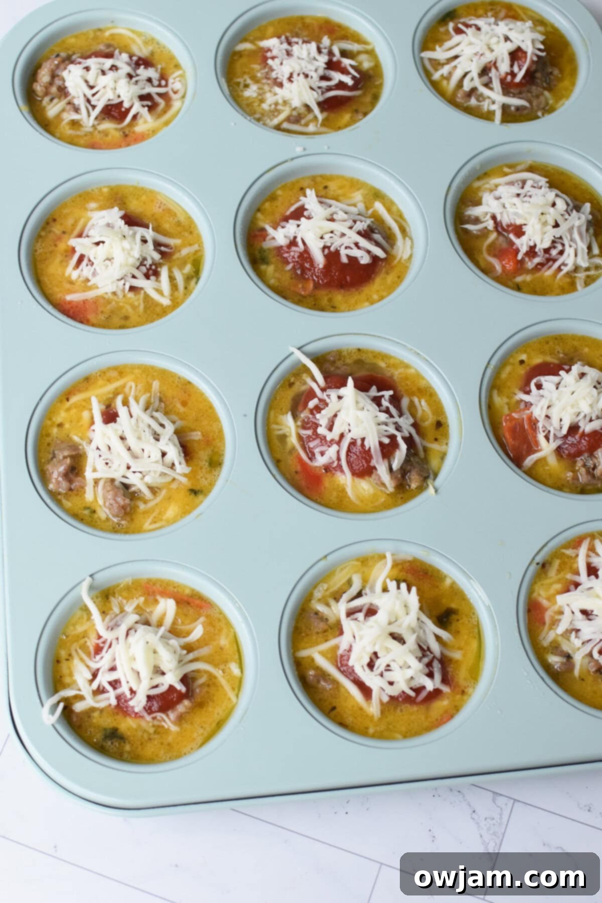 Cheesy Pizza Egg Bites 8 Unbaked Pizza Egg Muffins in a muffin tin with sauce and cheese topping