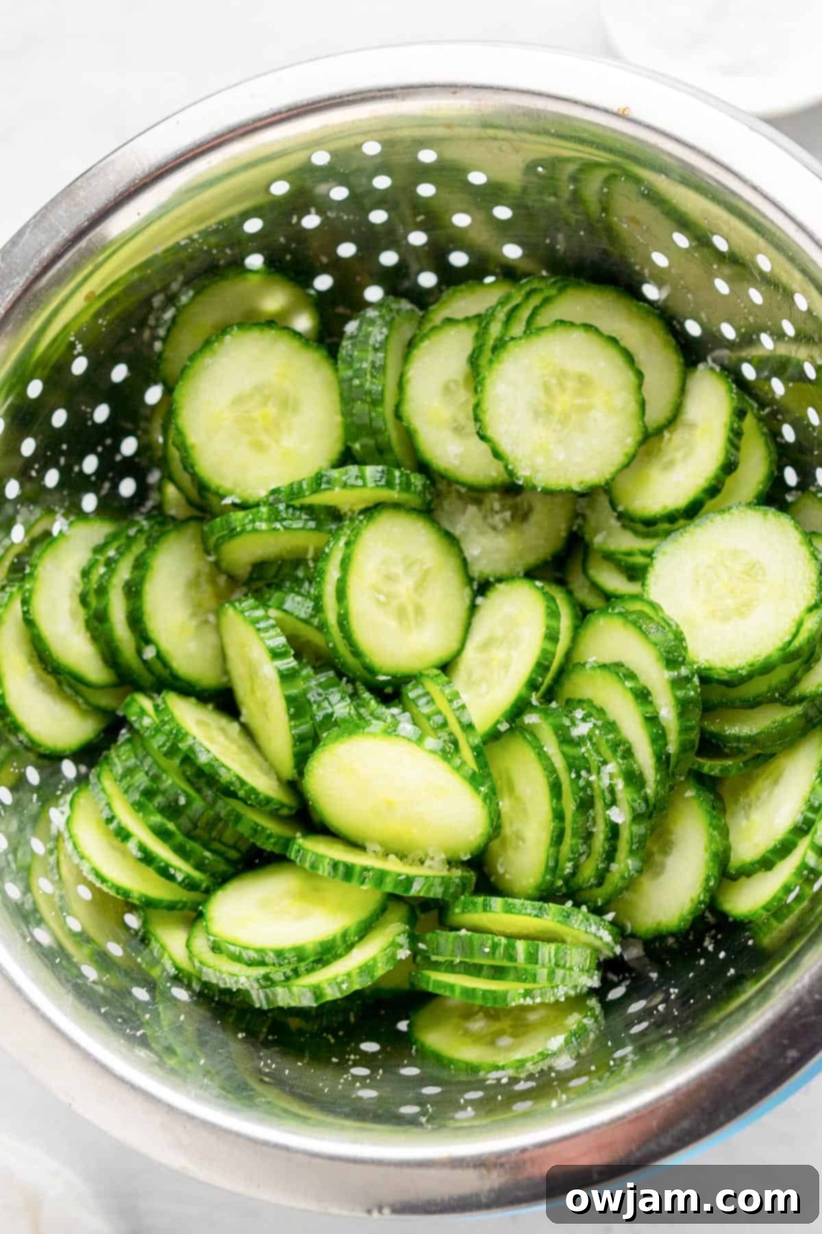 Salted and drained cucumber slices in a colander, illustrating the moisture removal step