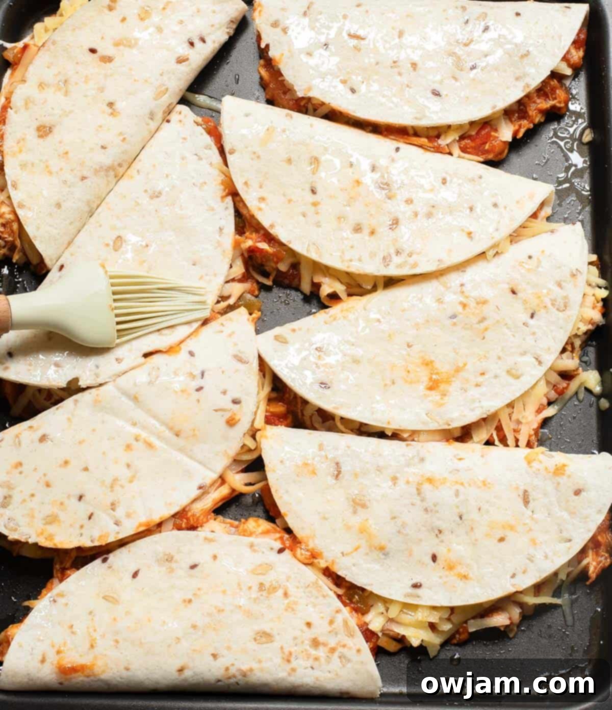 Baked Chicken Tacos lined up on a baking sheet, brushed with oil and ready for the oven