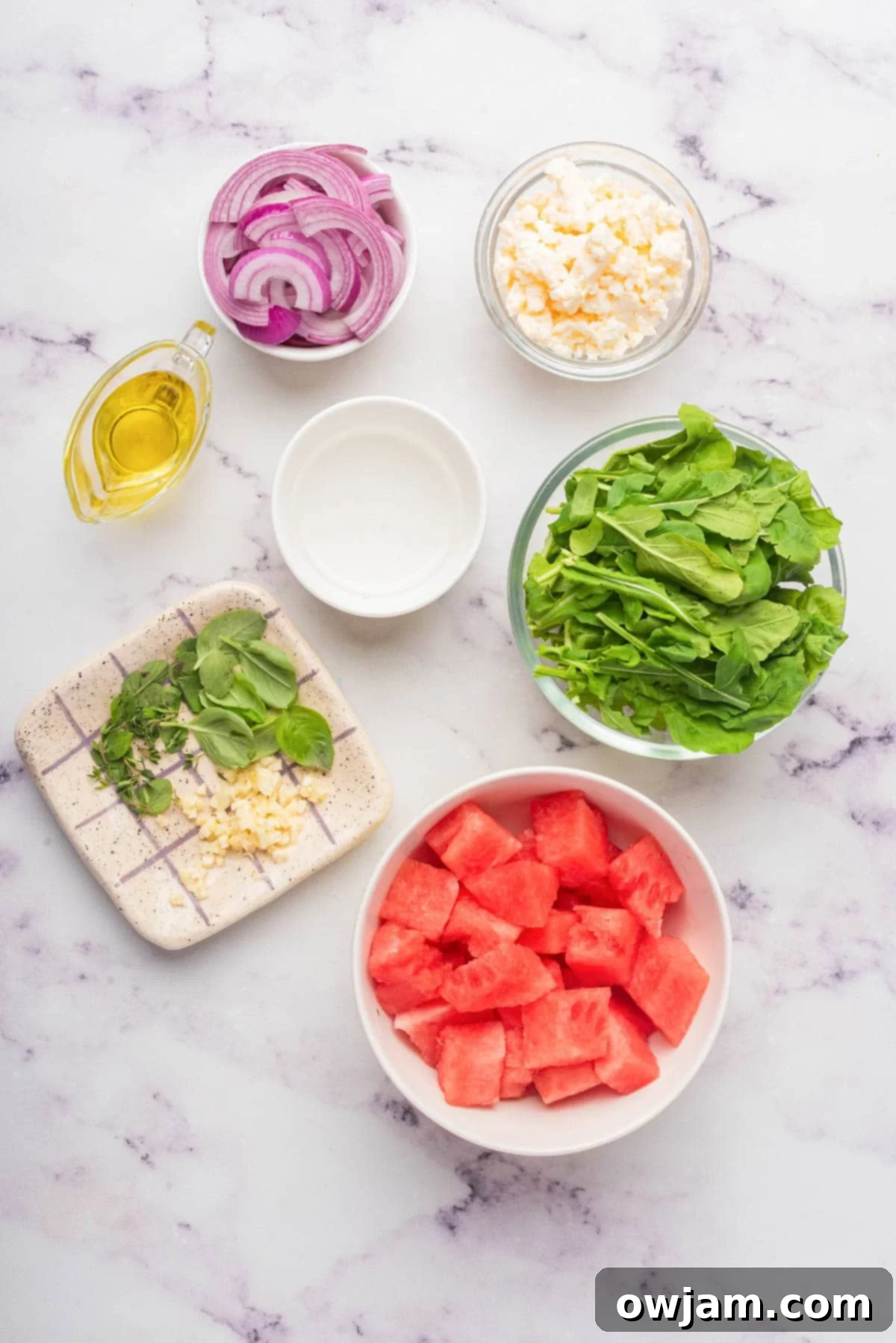 Close-up of fresh ingredients for Watermelon Arugula Salad, including watermelon cubes, arugula, feta, and red onion.