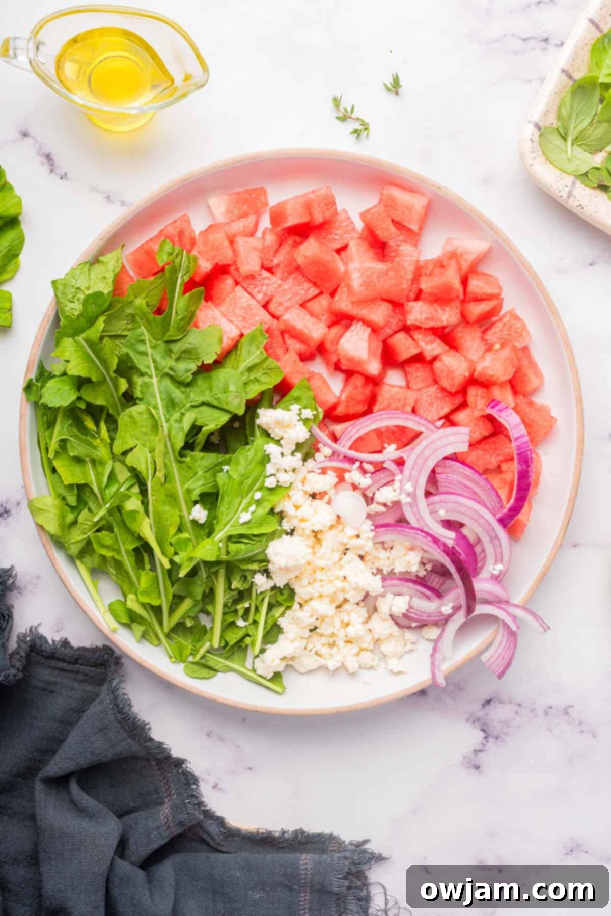 Close-up of watermelon, arugula, and feta being combined in a large bowl, ready for dressing.