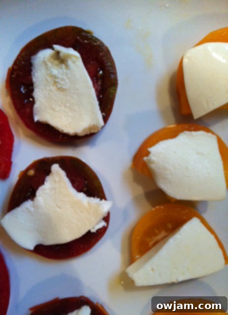 Assembling the Heirloom Caprese Salad with alternating layers of tomato, mozzarella, and basil