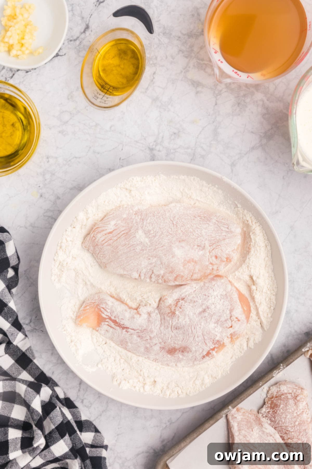 Chicken cutlets being dredged in flour on a plate, ready for browning.