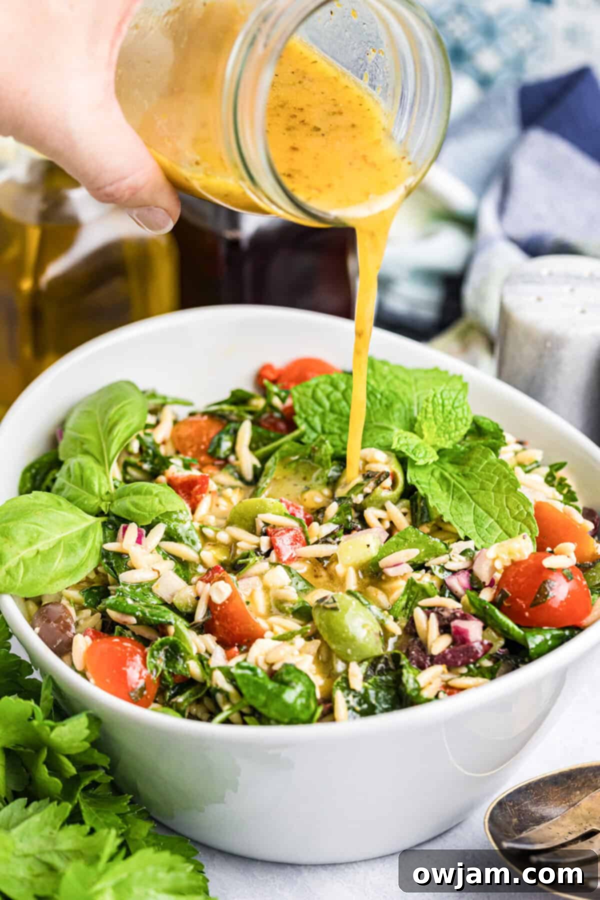 Sun-Kissed Mediterranean Pasta Bowl 8 Zesty Greek dressing being poured over a Mediterranean Pasta Salad in a large bowl.