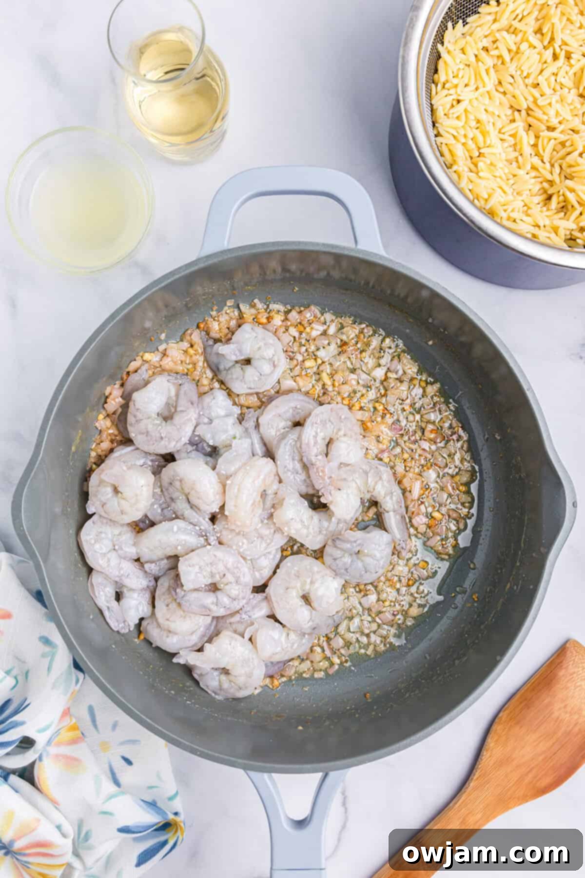 Zesty Lemon Shrimp with Orzo 7 Raw shrimp cooking in a skillet with sautéed garlic and shallots, turning pink