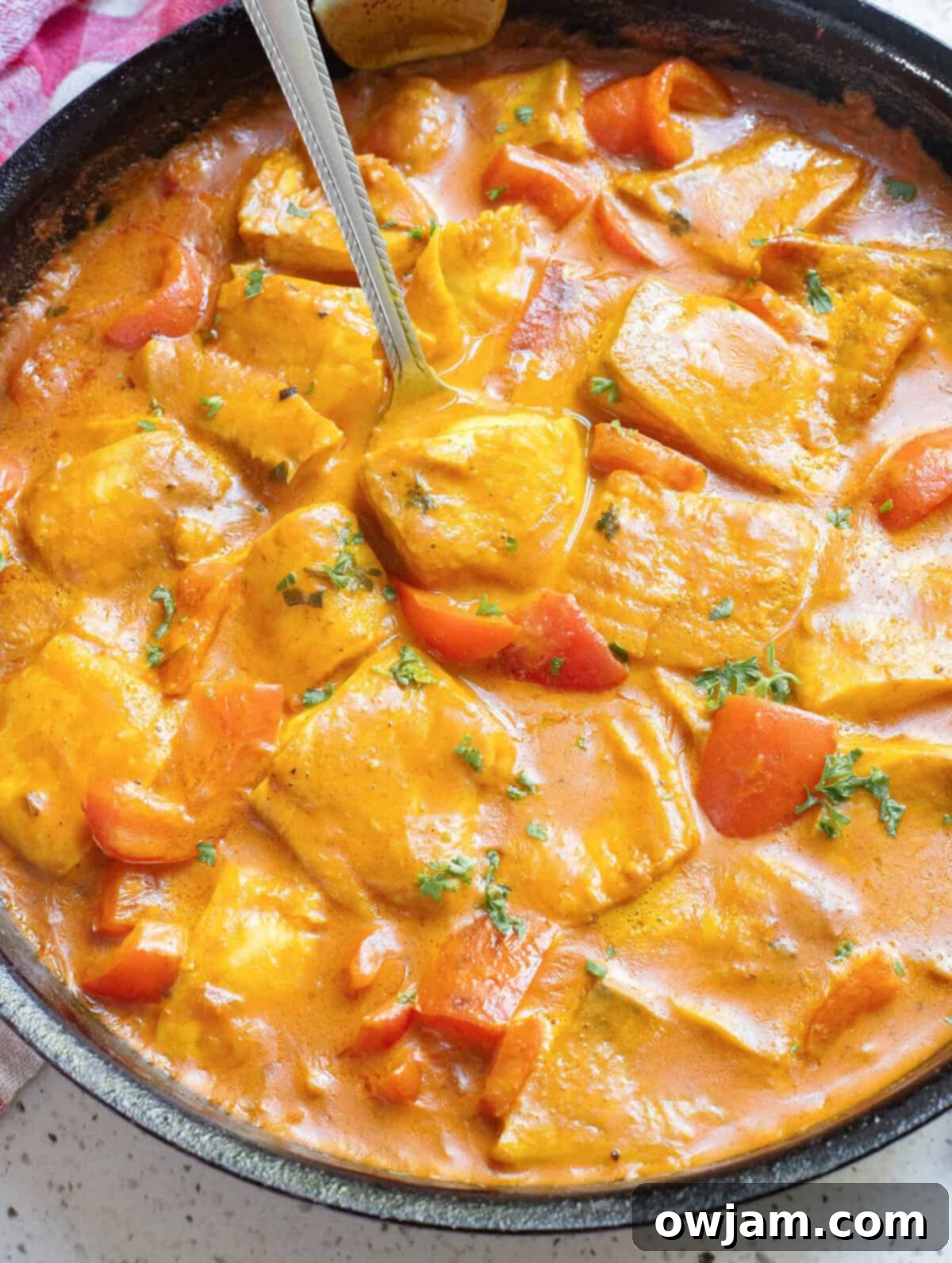 Luscious Coconut Fish Curry 2 Coconut Fish Curry in a skillet with a spoon, garnished with fresh cilantro.