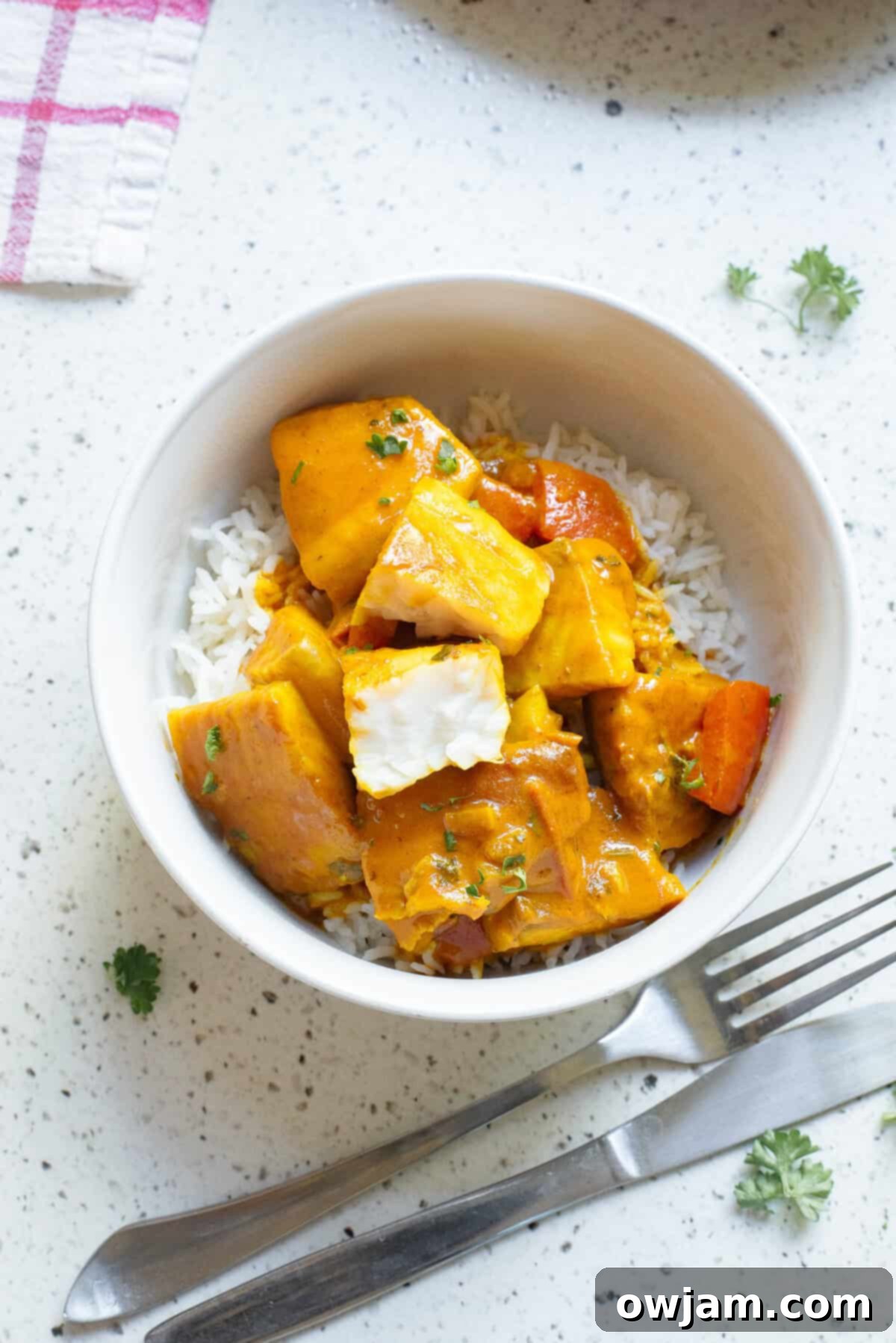 Luscious Coconut Fish Curry 9 A serving of Coconut Fish Curry in a white bowl, garnished with fresh cilantro and lime wedges.
