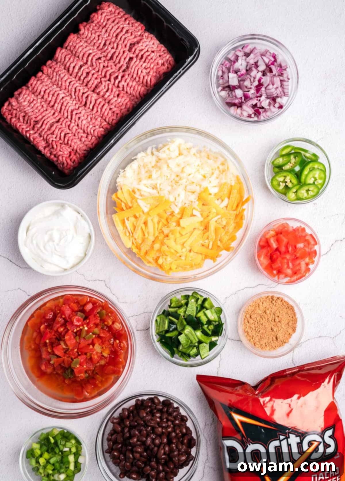 Various ingredients for Doritos Taco Casserole including ground beef, diced peppers, seasoning, cheese, and a bag of Doritos.
