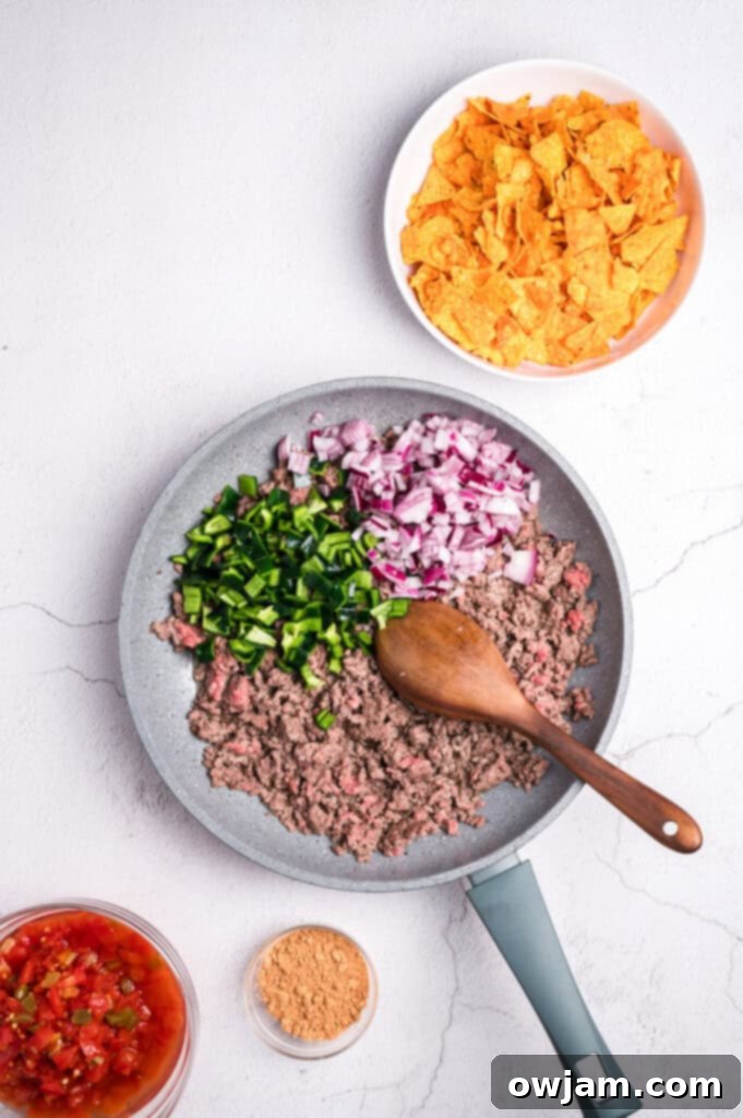 Ground beef cooking in a skillet, being broken up with a spoon.