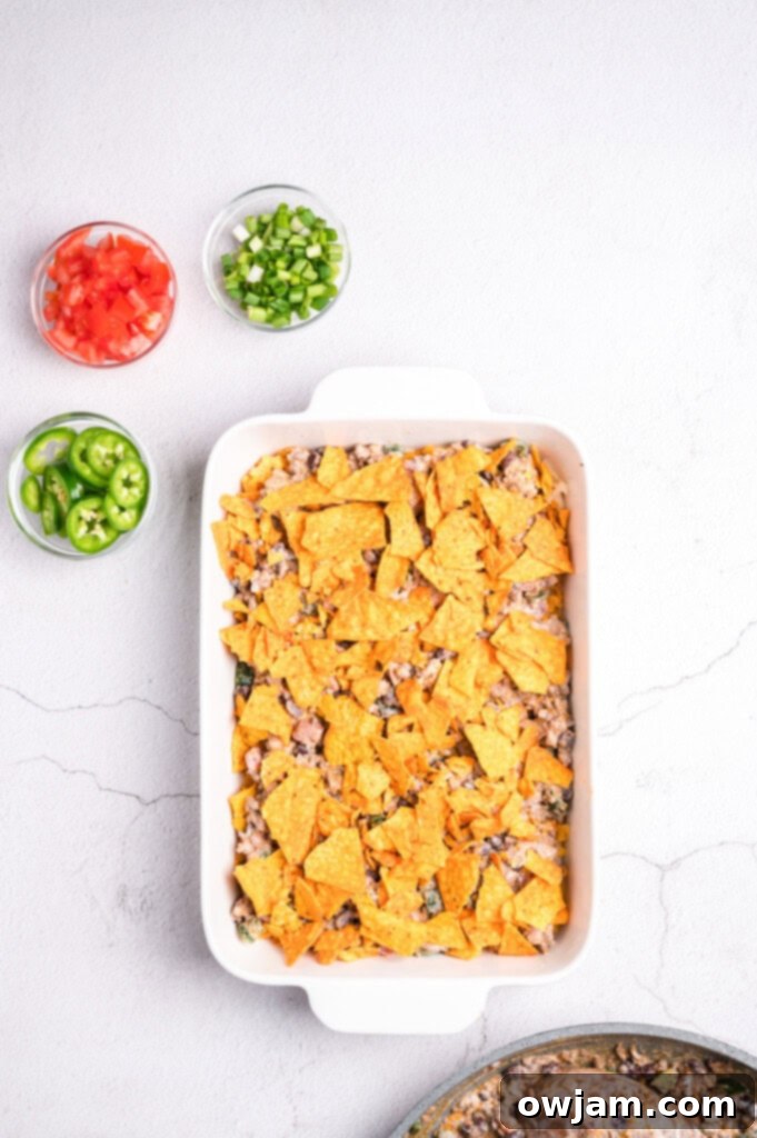Crushed Doritos being layered over the beef mixture in the baking dish.