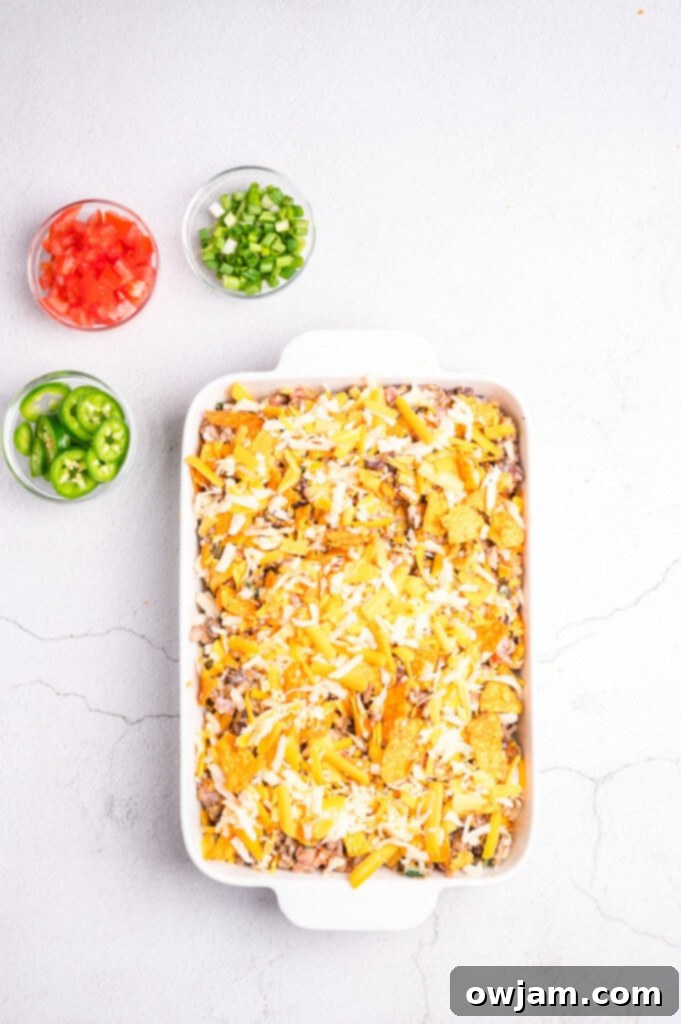 The Doritos Taco Casserole fully assembled in the baking dish, topped with cheese and chips, ready for the oven.