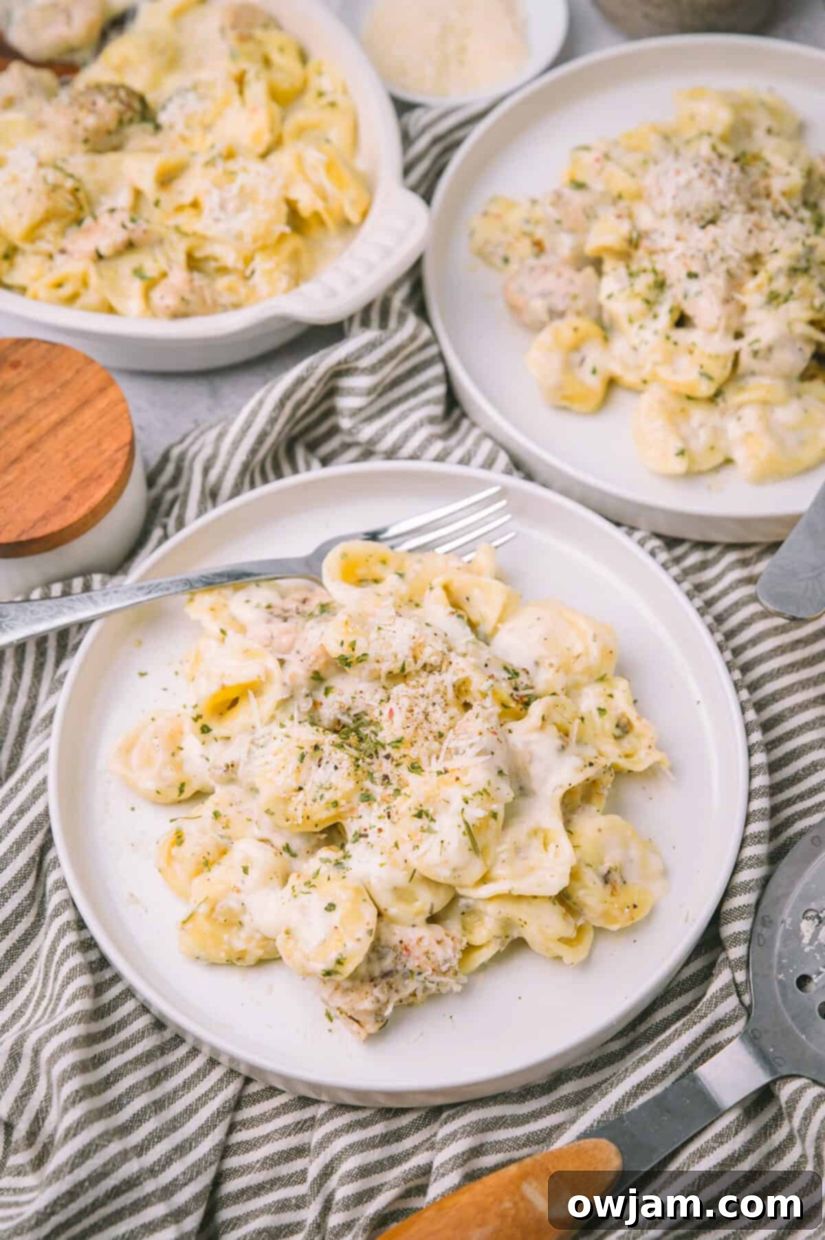 A serving of homemade Olive Garden Chicken Tortellini Alfredo on a white plate, garnished with fresh herbs.