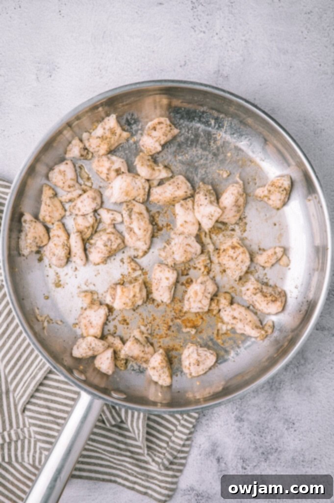 Close-up of diced chicken being seasoned in a bowl with olive oil and spices for Olive Garden Chicken Tortellini Alfredo.