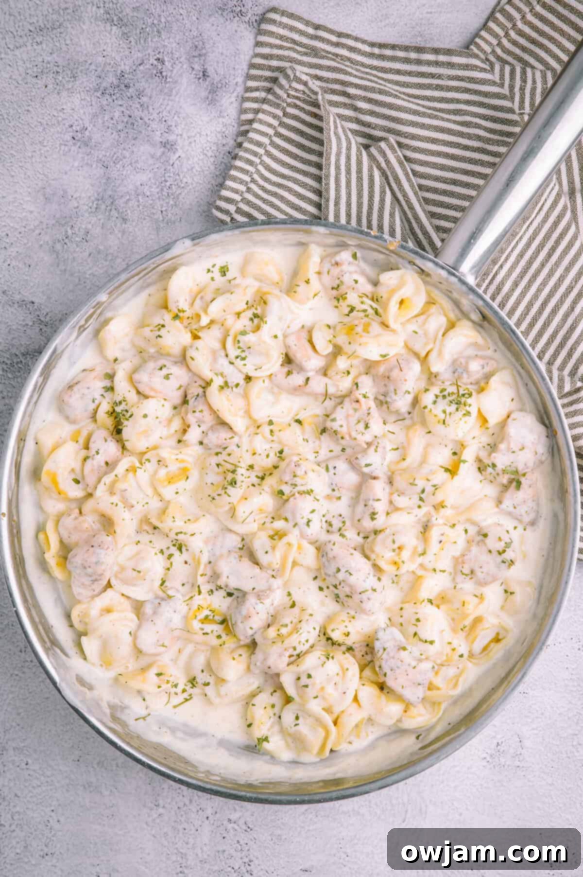 A large skillet brimming with Olive Garden Chicken Tortellini Alfredo, garnished and ready.