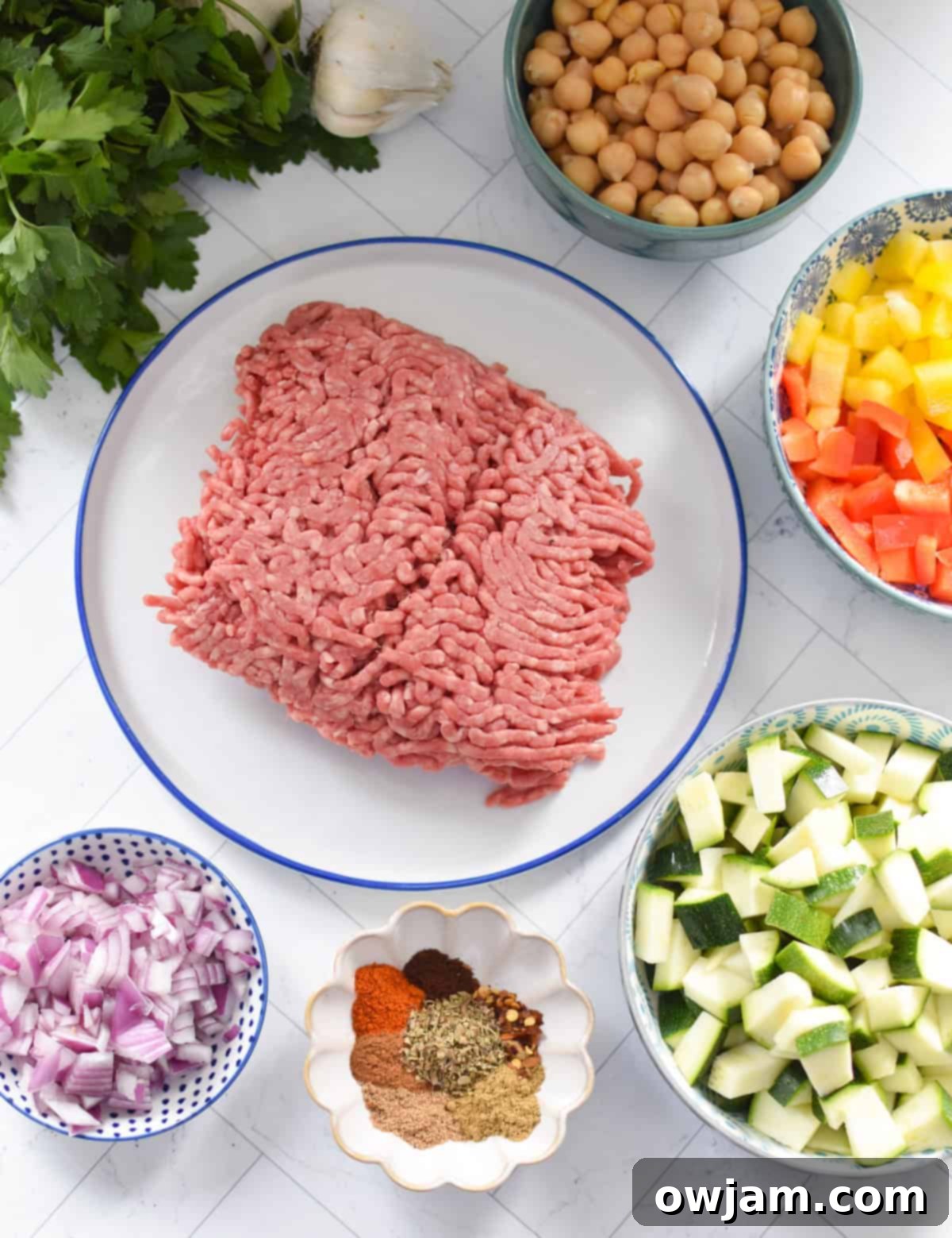 A collection of fresh ingredients laid out for the Mediterranean Ground Beef Skillet: bell peppers, zucchini, tomatoes, chickpeas, ground beef, and various spices