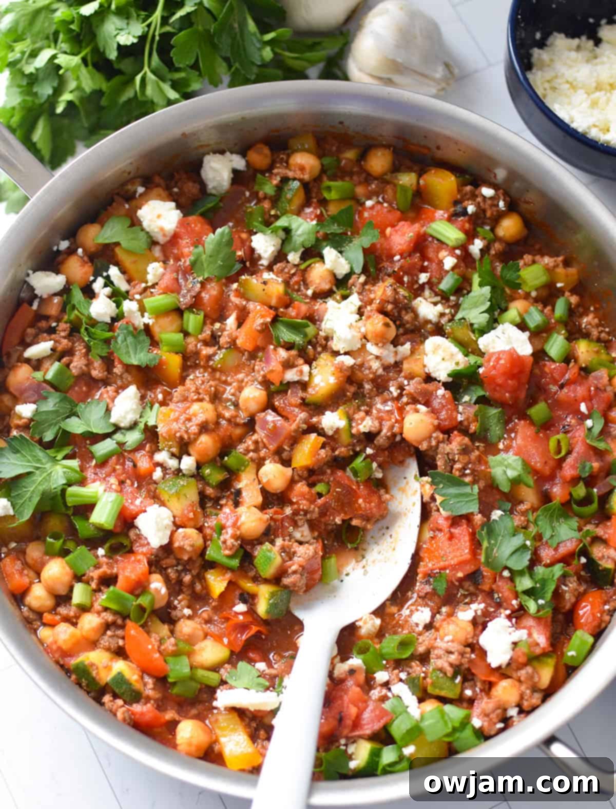 A close-up of the finished Mediterranean Ground Beef Skillet, with a white serving spoon resting in the mix of beef, vegetables, and herbs