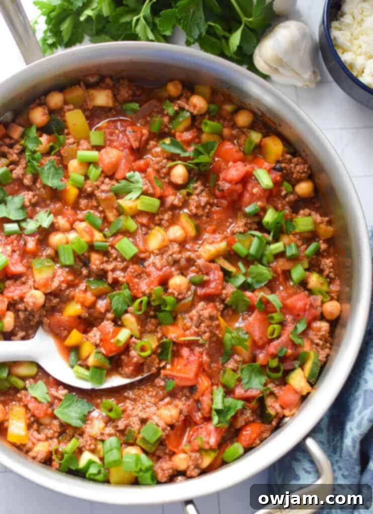 A bowl of Mediterranean Ground Beef Skillet, garnished with fresh herbs and feta, ready to eat, with a spoon in it