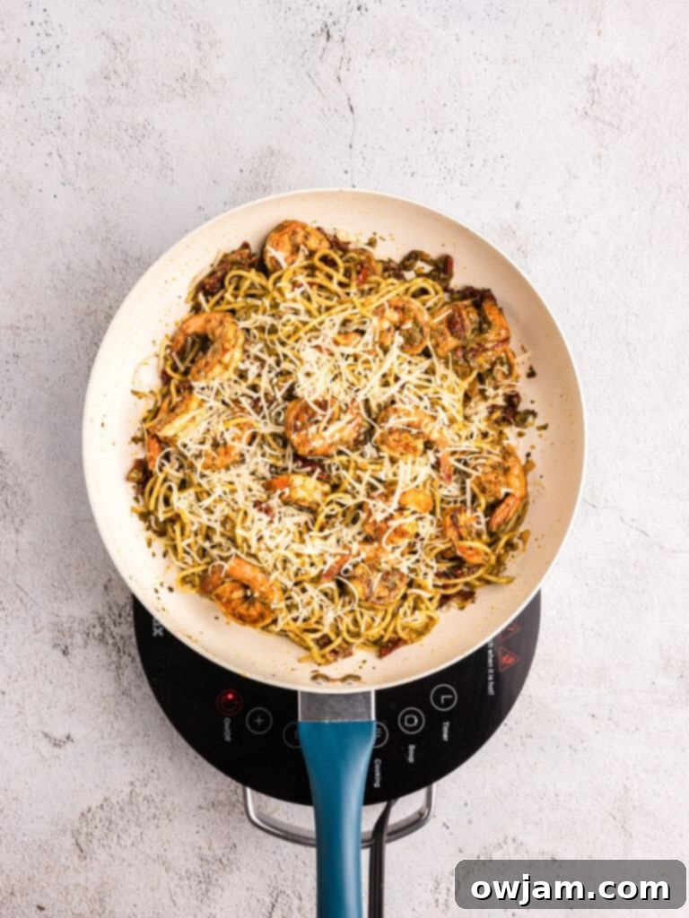 Pasta, shrimp, sun-dried tomatoes, and pesto being tossed in a pan