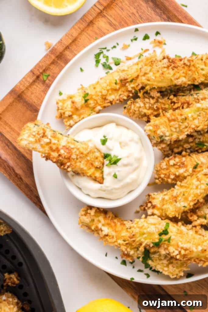 Crispy Air Fryer Zucchini Sticks 6 Air Fryer Zucchini Fries on a plate with dipping sauce, garnished with fresh parsley.
