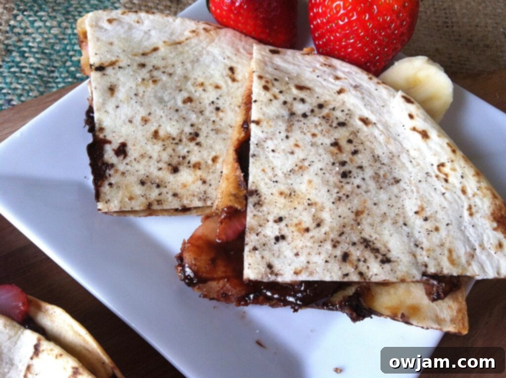 Delicious Dessert Quesadilla slices on a white plate, showcasing melted chocolate, bananas, and strawberries.