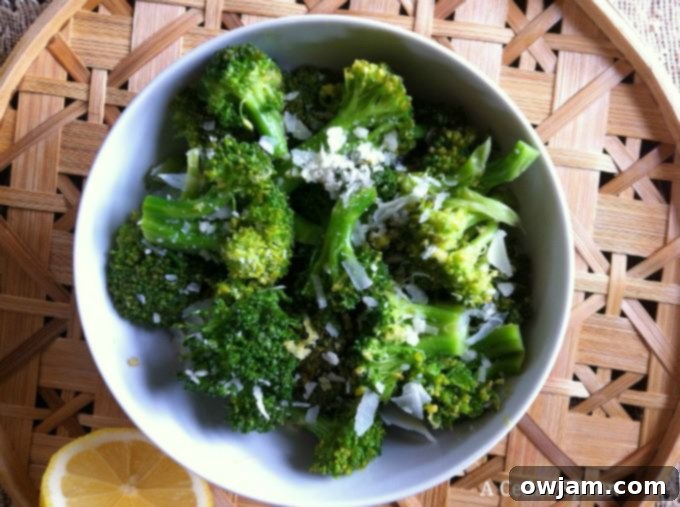 A closer look at a serving of Lemon Parmesan Broccoli in a white bowl, showcasing the vibrant green florets coated with cheese and lemon zest, ready for a meal.