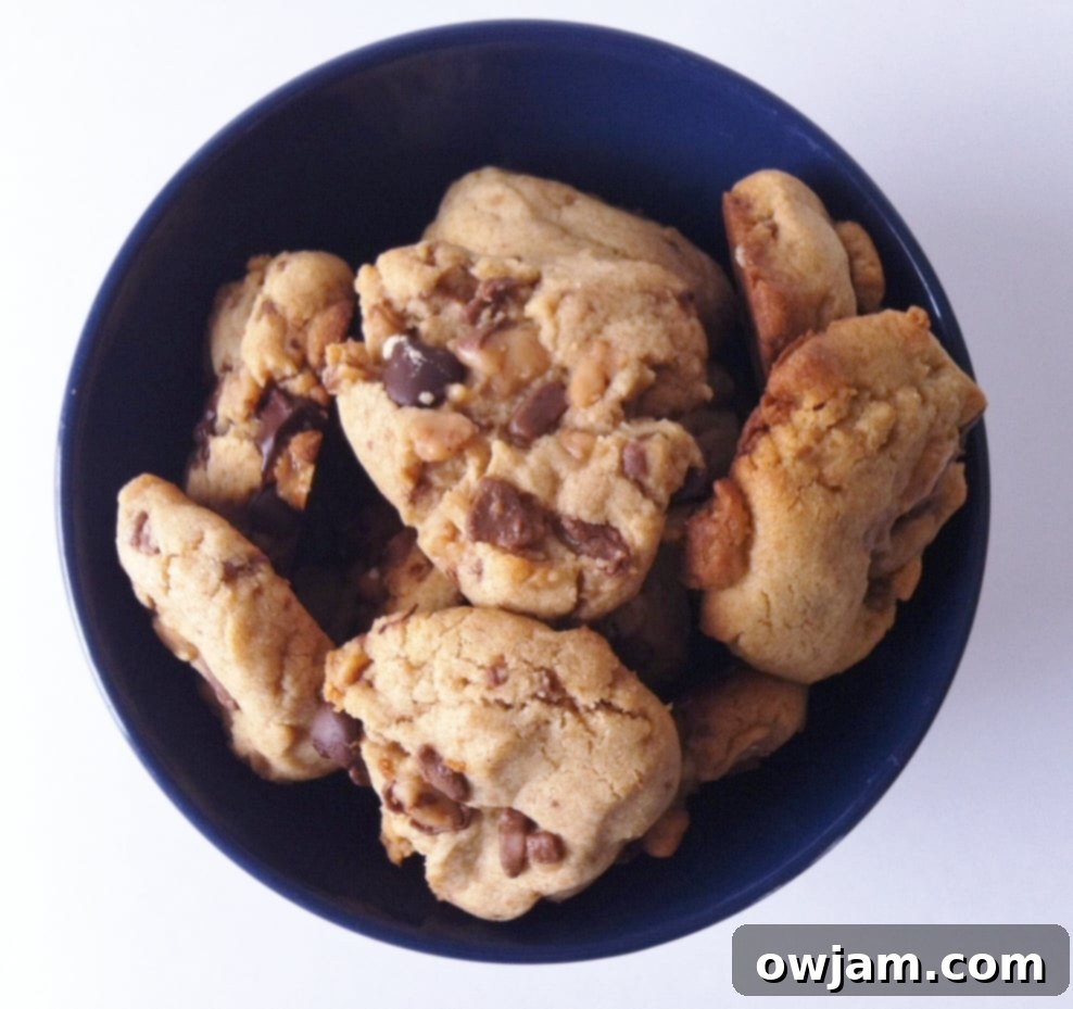 A bowl overflowing with golden brown Peanut Butter Toffee Cookies, speckled with melted toffee