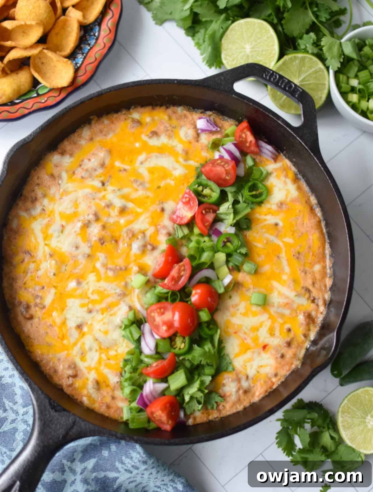 Beefy Cottage Cheese Queso 4 Cottage cheese beef dip baked in a black cast iron skillet and garnished with diced tomatoes, green onion, cilantro and red onions up above with chips on a plate.