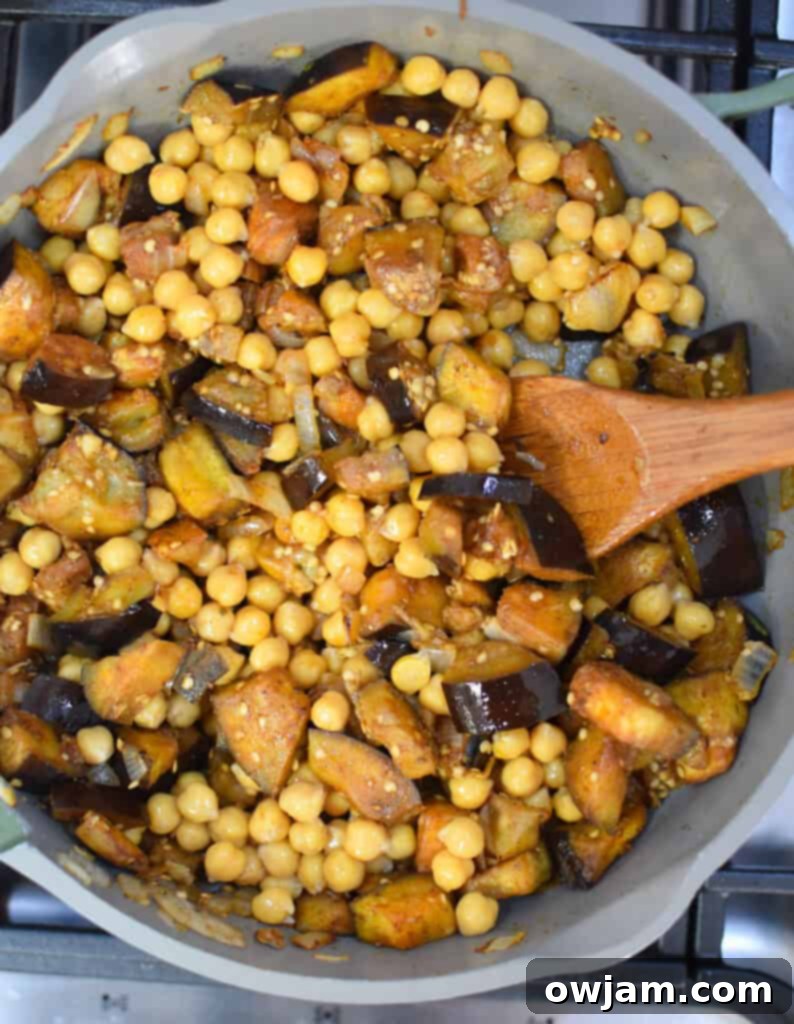 Lebanese Moussaka Maghmour 7 Eggplant, chickpeas, and diced tomatoes simmering together in a skillet, creating a rich and aromatic Lebanese Moussaka base.
