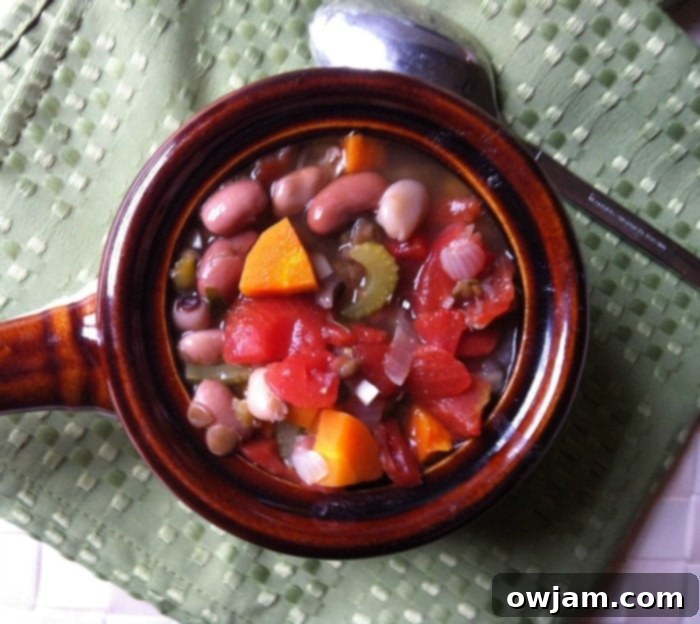 A close-up view of a large pot of homemade vegetarian 15 bean soup simmering on the stovetop, rich with beans and vegetables.