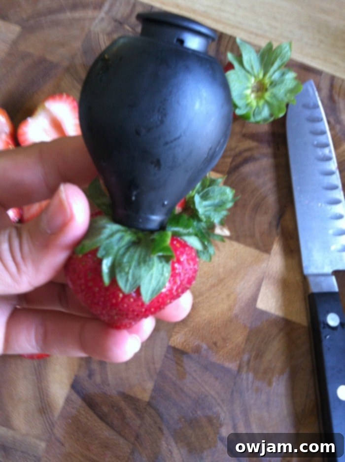 Close-up of the OXO strawberry huller tool, demonstrating its ease of use in preparing fresh strawberries.