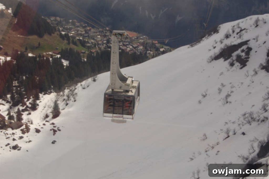 A cable car ascending a steep mountain face in the Swiss Alps, with dramatic peaks visible in the distance.