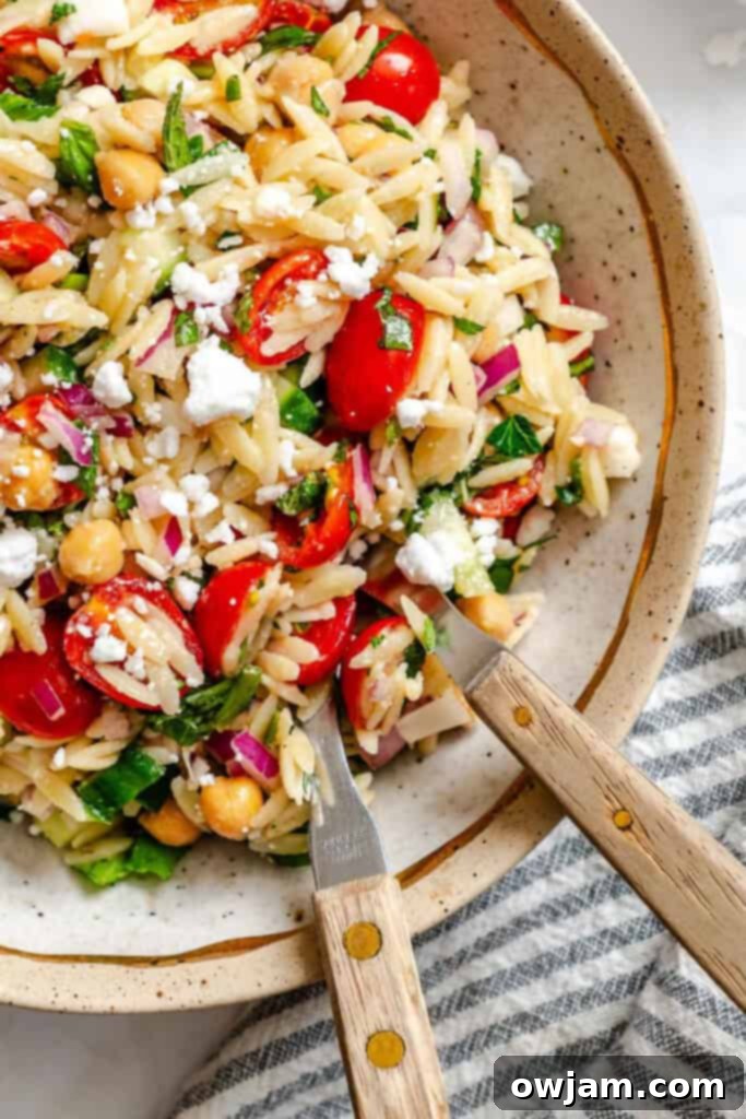 Summer Orzo Pasta Salad in a bowl with two spoons, showcasing its vibrant colors and fresh ingredients.