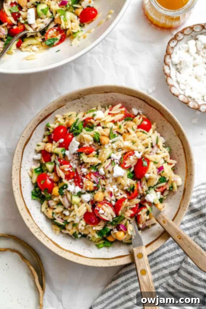 A bowl of Summer Orzo Pasta Salad with a fork and spoon, ready for serving.