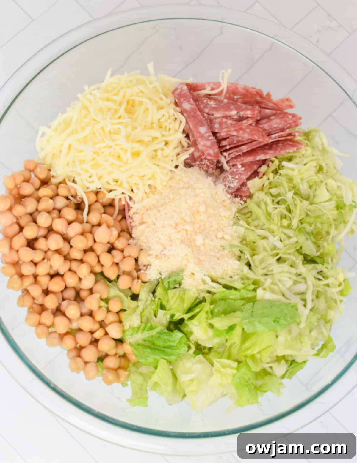La Scala Style Chopped Salad Made at Home 8 Finely chopped romaine and iceberg lettuce, salami, chickpeas, and mozzarella cheese mixed in a clear glass bowl, ready for dressing.