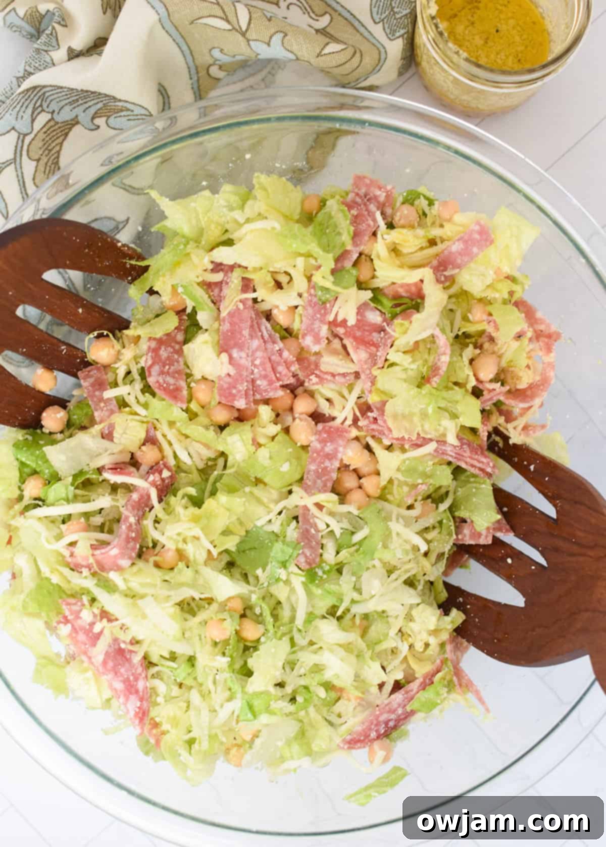 La Scala Style Chopped Salad Made at Home 10 Finished Copycat La Scala Chopped Salad in a clear glass bowl with wooden serving spoons, garnished with fresh parmesan.
