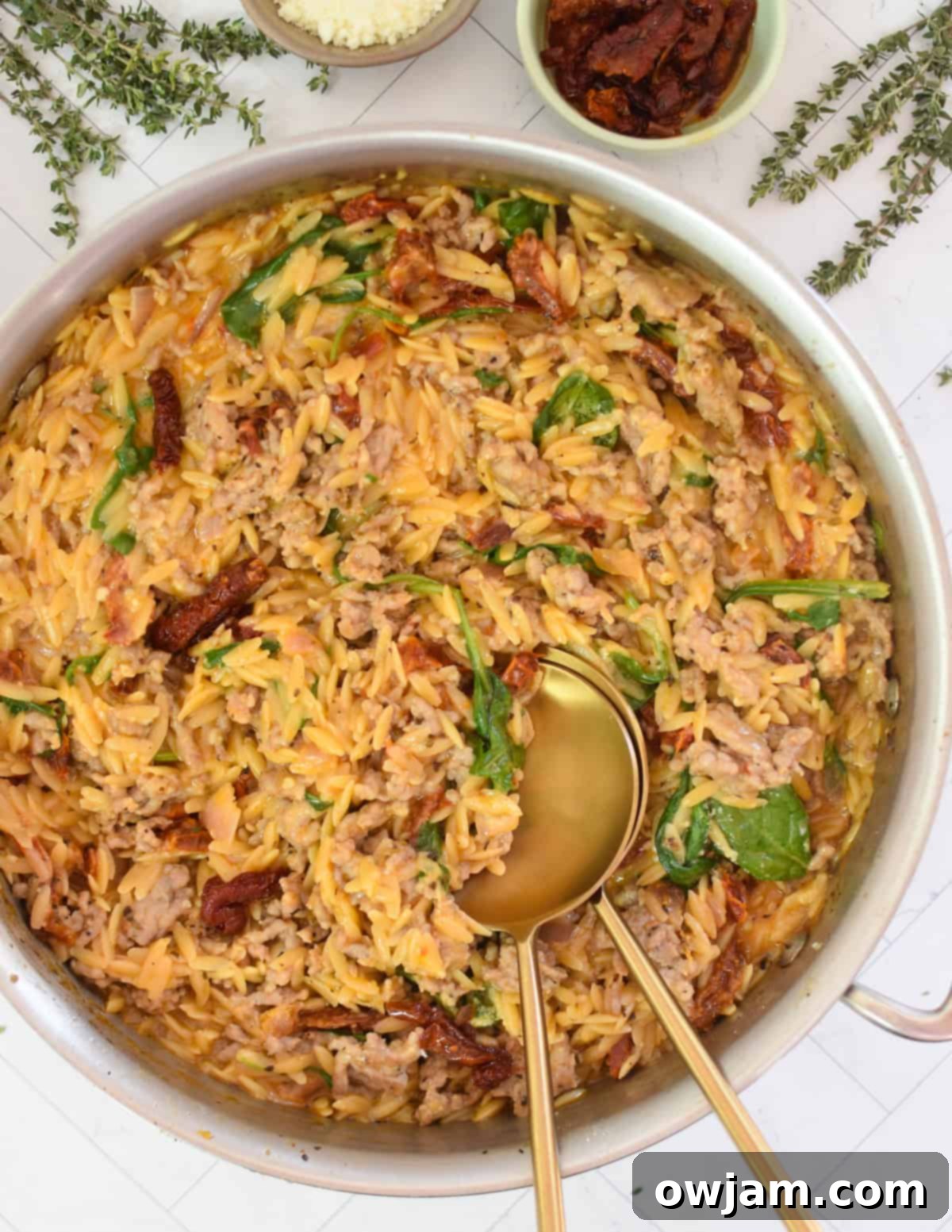 Creamy One Pot Sausage Orzo in a cast iron skillet with golden spoons resting in it, ready to be served.