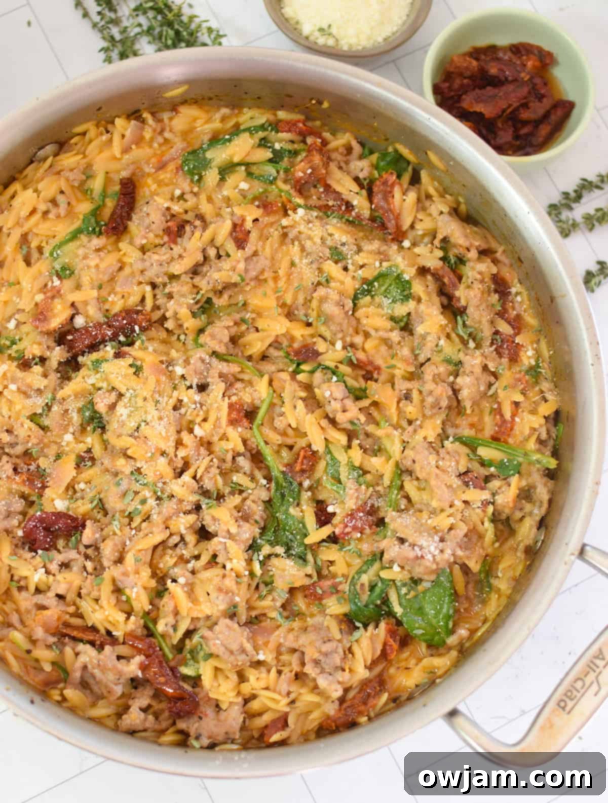 One Pot Sausage Orzo in a silver skillet, garnished with fresh Parmesan cheese and herbs, ready to be served.