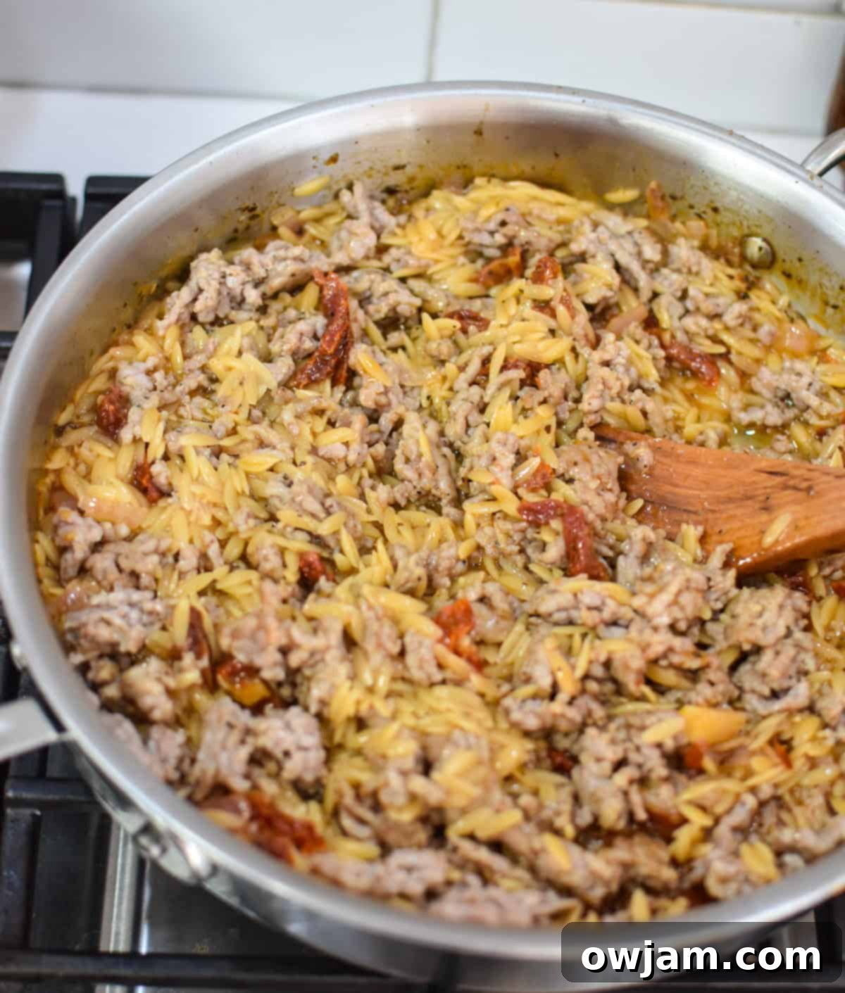 Italian sausage being browned and cooked in a skillet with spices for the One Pot Sausage Orzo recipe.