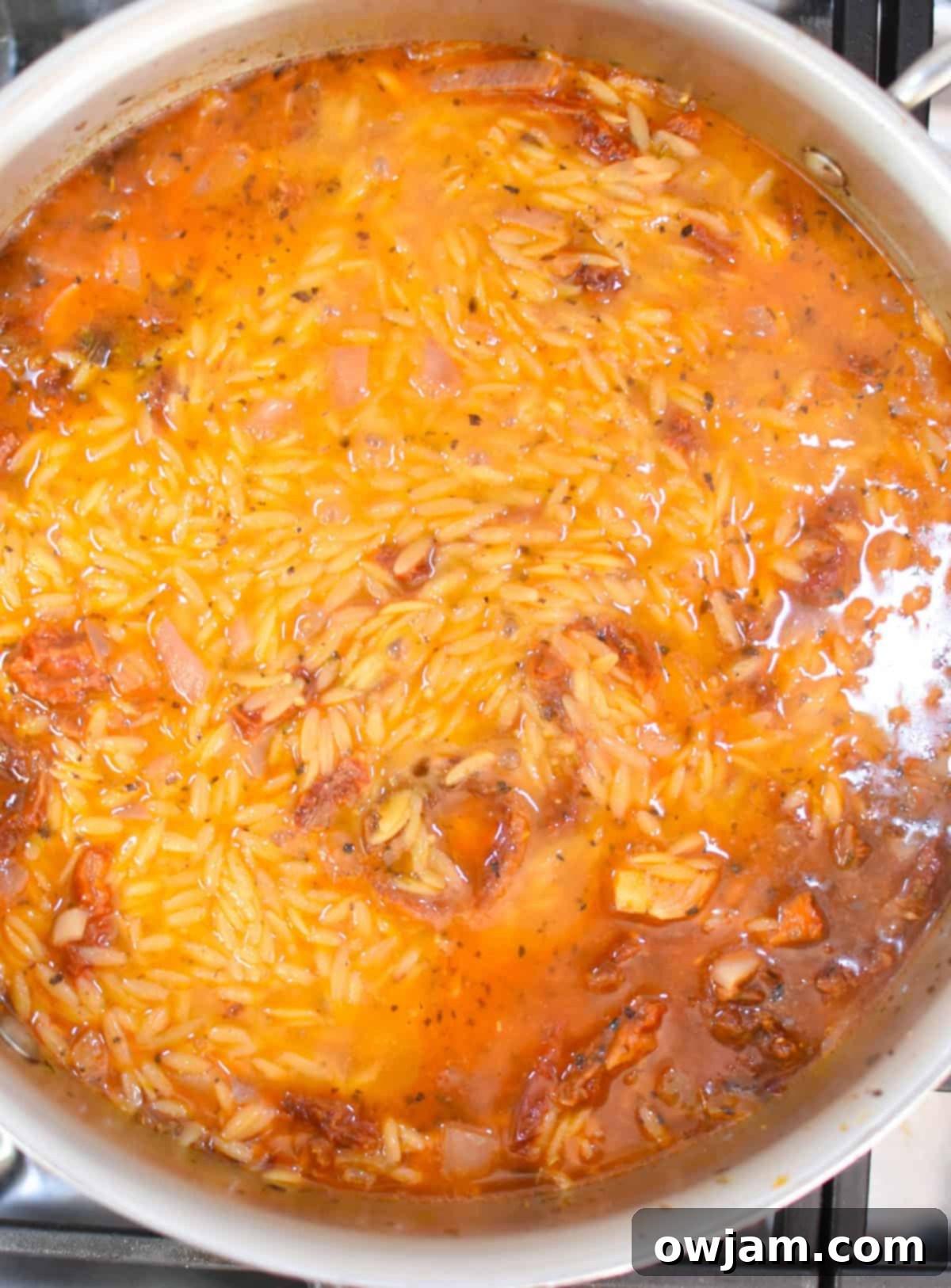 Orzo and broth simmering in the same skillet after the sausage has been cooked and removed, preparing for the creamy One Pot Sausage Orzo.