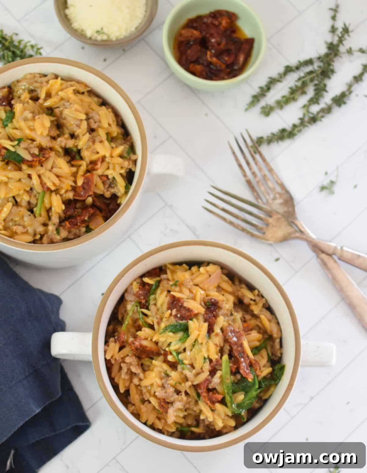 Two small white bowls filled with creamy One Pot Sausage Orzo, garnished with fresh herbs, ready to eat.